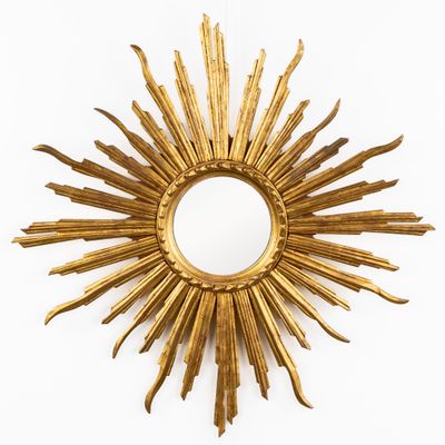 une photo représentant un miroir doré en forme de soleil rayonnant accroché à un mur blanc