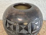 a silver vase sitting on a table with a white wall behind it
