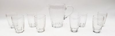 sept verres et un pichet posés sur une surface blanche