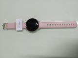 La montre rose est posée sur une surface blanche, à côté d'une étiquette blanche.