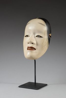 une image représentant un masque blanc posé sur un socle noir, sur fond gris