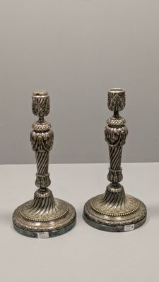 deux bougeoirs en argent posés sur une table blanche, sur fond gris