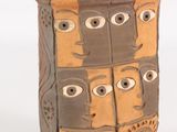 un vase marron orné de visages sur un fond blanc