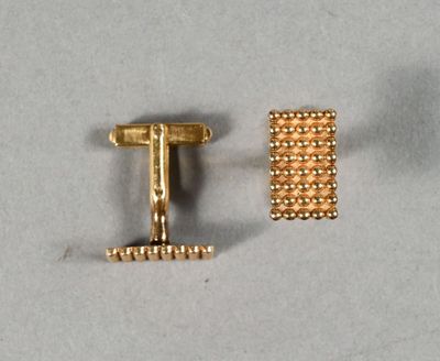 une paire de boutons de manchette en or posés sur une surface blanche