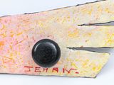 a close up of a piece of art with a black button on it