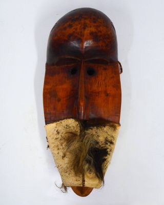 un vieux masque en bois posé sur une surface blanche, avec une longue barbe