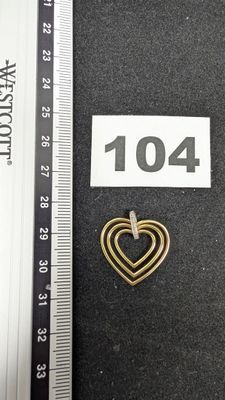 une photo d'une broche en forme de cœur doré avec une règle en arrière-plan
