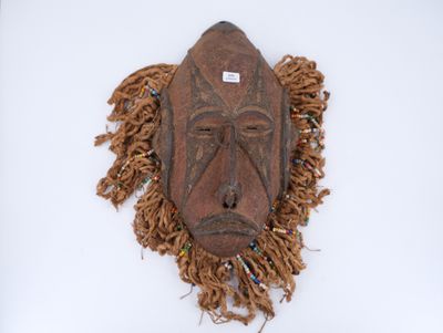 un vieux masque en bois orné de franges sur un fond blanc