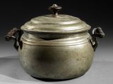 une vieille casserole en métal avec un couvercle et des poignées, posée sur une table