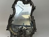 un miroir ancien au motif ouvragé, posé sur un socle, sur fond blanc
