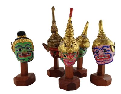 trois masques de couleurs différentes posés sur des socles en bois, sur un fond blanc