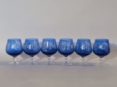 six verres à vin bleus alignés sur une surface blanche