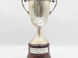 trophée en argent posé sur un socle en bois, sur fond blanc, avec un espace réservé au texte