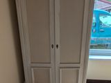 une armoire blanche dans un coin de la pièce, près d'une fenêtre