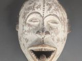 un masque en bois accroché au mur, sur lequel se dessine un sourire
