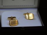 two pairs of gold cufflinks in a box on a black surface