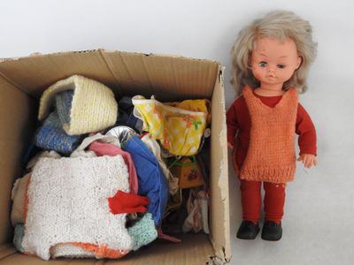 une poupée debout à côté d'un carton rempli de vêtements