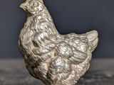 a silver figurine of a chicken on a table