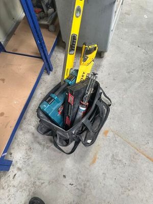 a tool bag with tools on the floor next to a pair of shoes