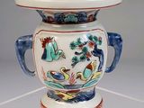 un vase blanc muni d'une anse bleue et orné d'un motif représentant un oiseau