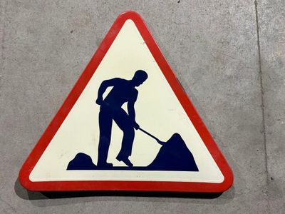 un panneau triangulaire sur lequel figure l'image d'un homme en train de pelleter de la terre