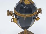 a black and gold vase on a stand on a white surface