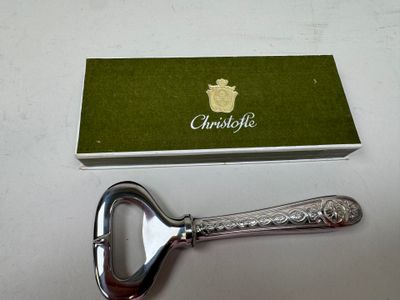 a silver bottle opener with a green box on a table