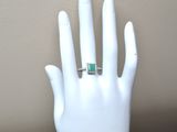 a hand with a ring on it that has a green stone on it