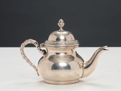 une théière ancienne en argent avec son couvercle, posée sur une table blanche