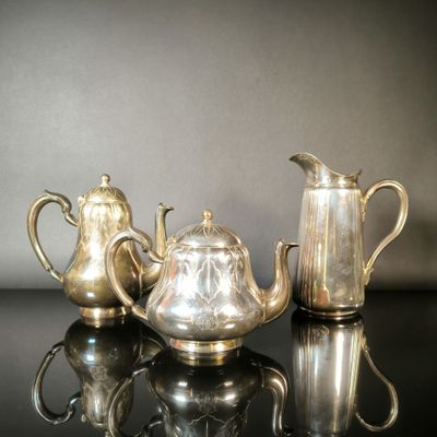 trois théières en argent et une cafetière posées sur une table