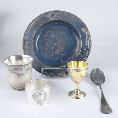 plusieurs objets en argent, dont une coupe, une cuillère et un repose-cuillère, posés sur une surface blanche