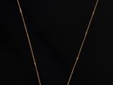a gold necklace with a white diamond pendant on a black background