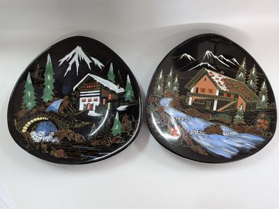two decorative plates with a cabin and a stream in the background