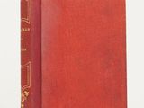un vieux livre rouge avec des bordures dorées posé sur une surface blanche