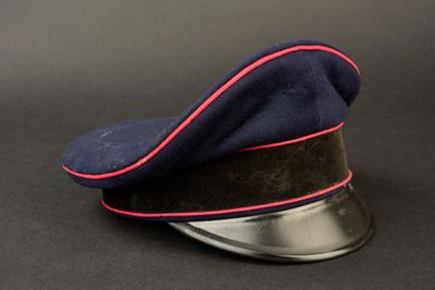 chapeau bleu marine avec une bordure rouge, posé sur une base métallique, sur fond noir