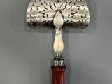 an antique silver plate with a wooden handle on a gray wall