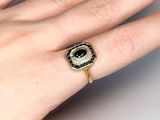 woman ' s hand wearing a gold ring with a black and white stone on it