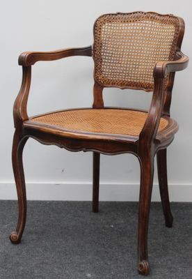 une photo d'une chaise en bois avec une assise en osier, posée sur un sol recouvert de moquette