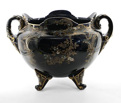 un vase noir et doré posé sur un socle, sur une surface blanche