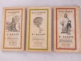 Trois brochures anciennes de salons français sont exposées sur une surface blanche