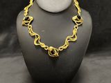 a gold plated necklace on a mannequin with a black background