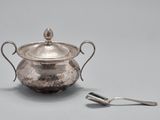 une casserole en argent posée sur une table, avec une cuillère à côté
