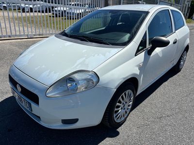 La petite voiture blanche est garée sur le parking, près d'une clôture.