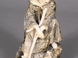 an old figurine of a man sitting on a rock with a stick