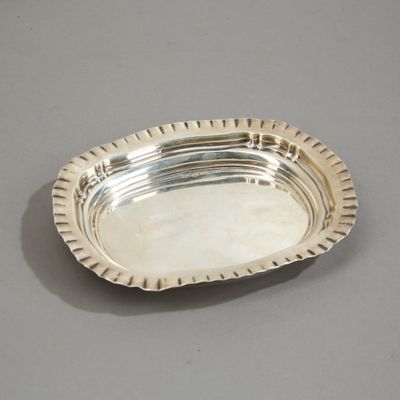 un plat ancien en argent posé sur un plateau gris et bordé d'argent