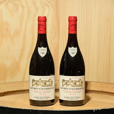 two bottles of red wine sitting on a barrel