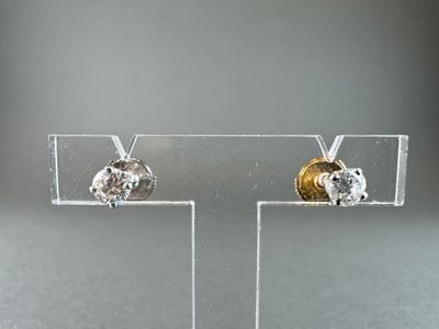 pair of gold and diamond stud earrings on clear acrylic stand