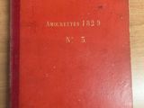 an old red book sitting on top of a wooden table next to a laptop