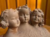 trois statues d'enfants assis sur un banc en bois