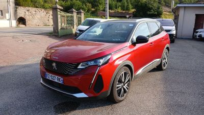 La voiture rouge est garée sur le parking, à côté d'autres voitures.